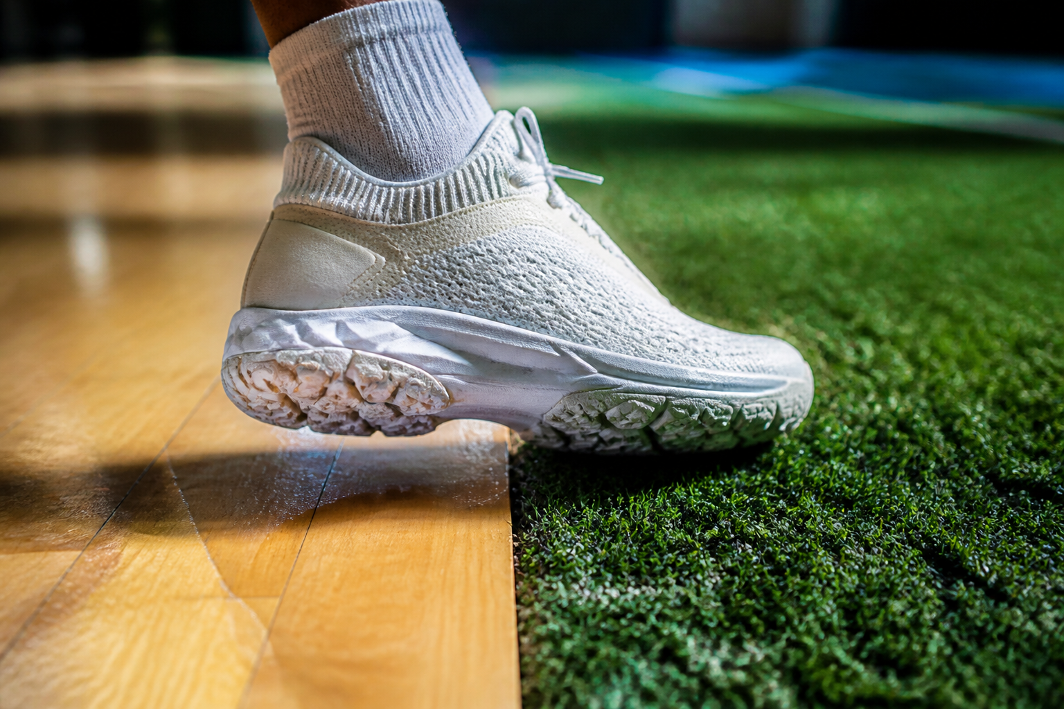 Hybride sportschoenen voor kunstgras en zaal op een gesplitst oppervlak van gras en hout.