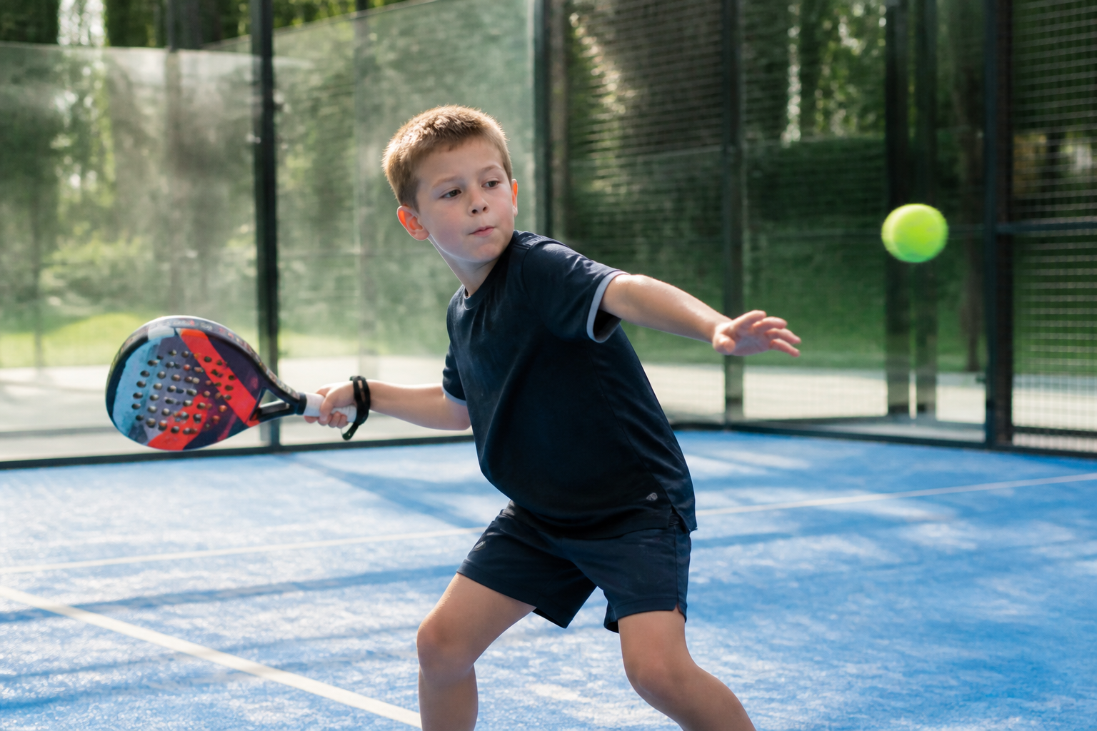 Kind op een blauwe baan met een specifiek padelracket voor kinderen tijdens een sportieve training.