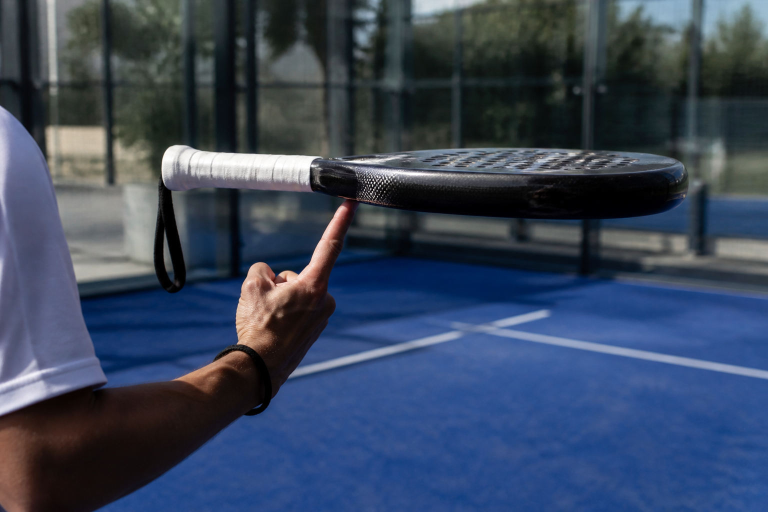 Close-up van een padelracket dat balanceert op een vinger om de balans padelracket te bepalen op een blauwe baan.
