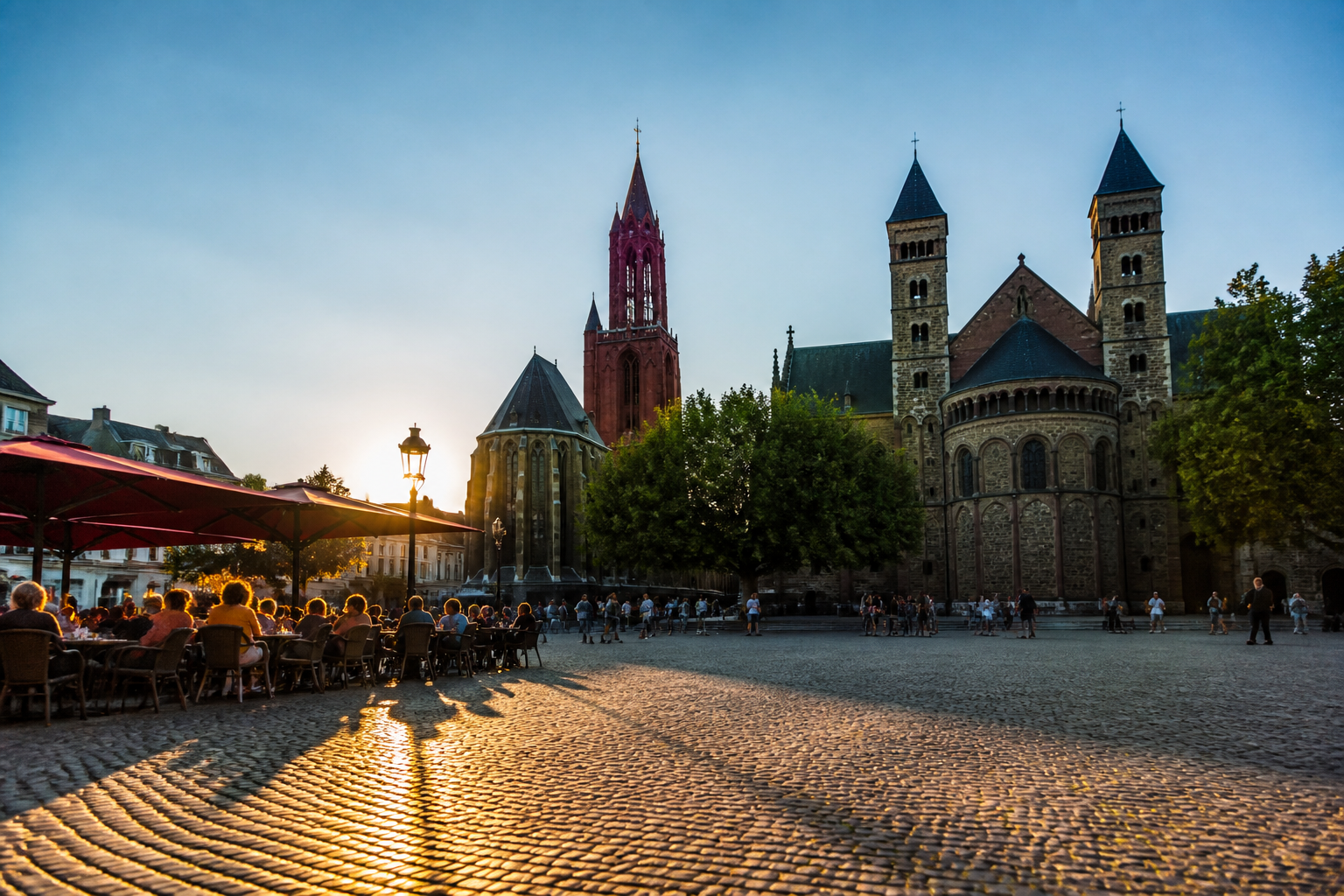 Overzicht van het Vrijthof plein in Maastricht met historische kerken en terrassen bij zonsondergang.